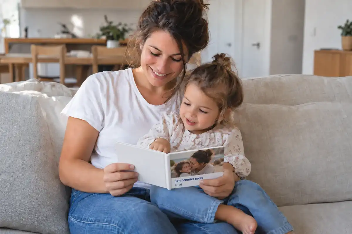 Une maman et son enfant feuillettent un petit livre photo sur leur canapé